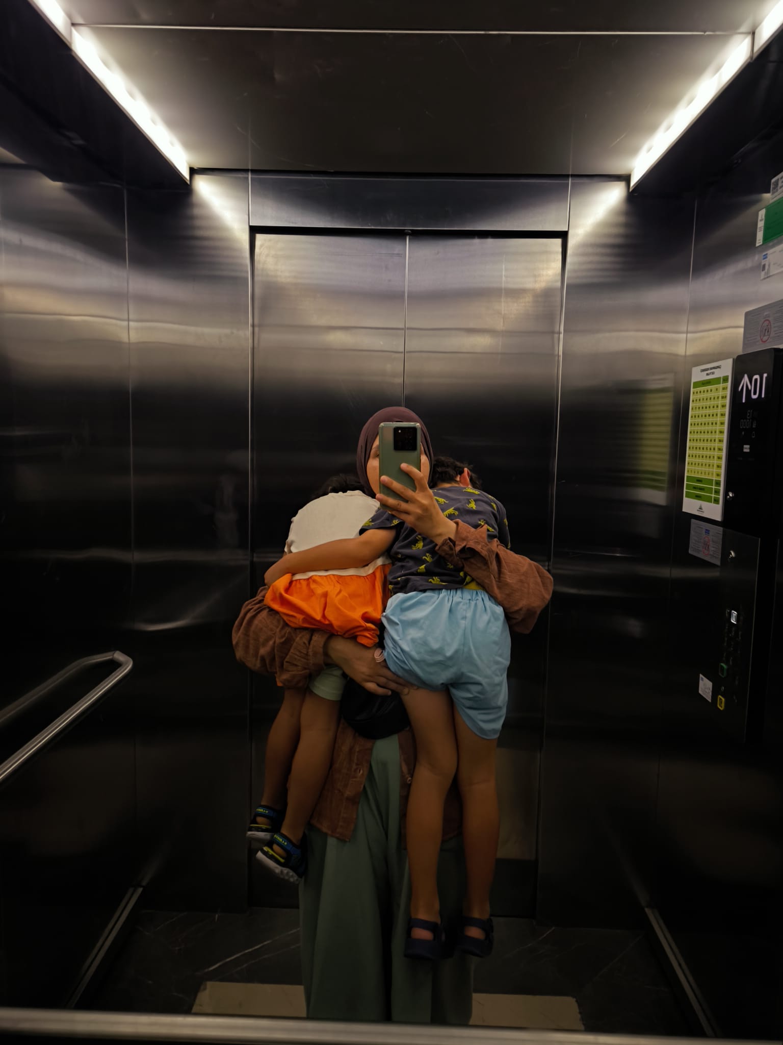 Kucağında iki çocuğuyla asansör aynasında selfie çeken bir anne